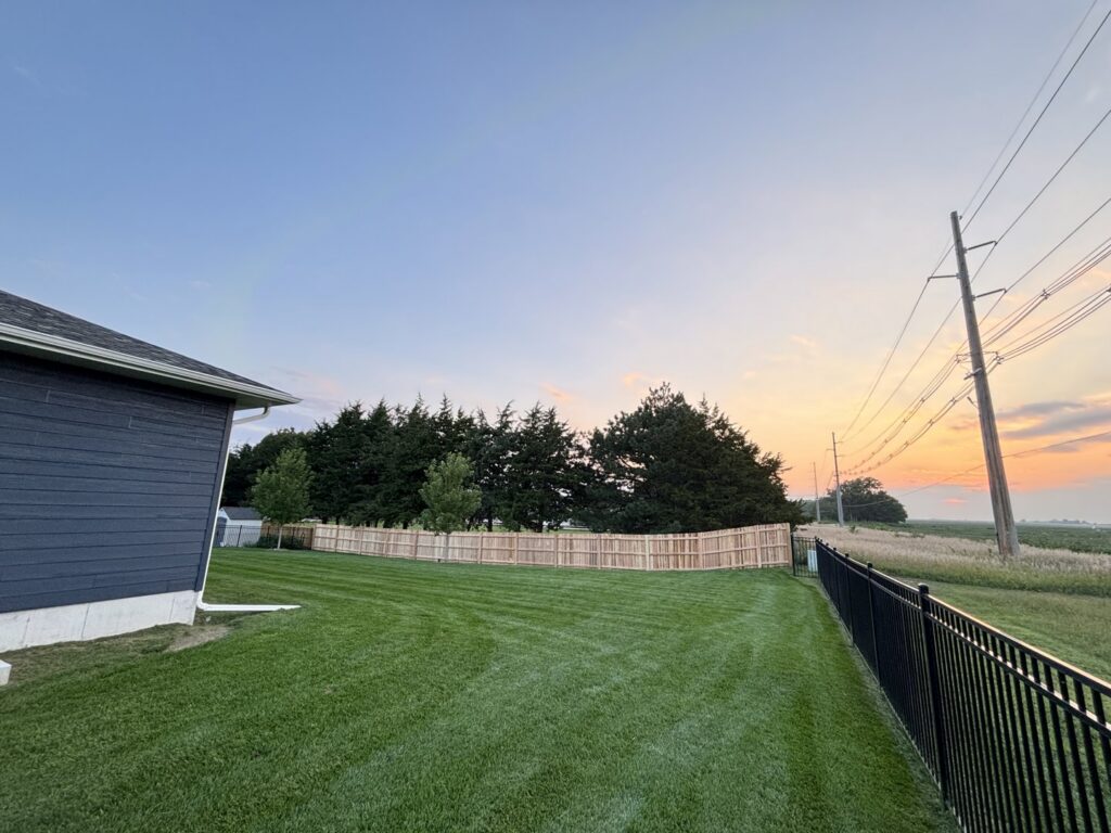 A long wood privacy fence and a black metal fence installed in a spacious backyard by American Fence Company of Norfolk in Grand Island, NE.