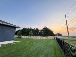 A long wood privacy fence and a black metal fence installed in a spacious backyard by American Fence Company of Norfolk in Grand Island, NE.