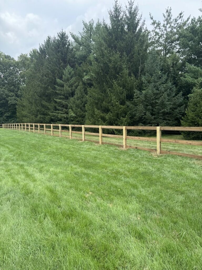 A long stretch of new wood and wire mesh fence in a large grassy field, installed by ReliableFencing in Columbus, OH.