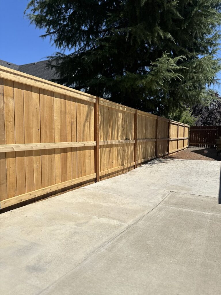 A long, newly installed wood fence running parallel to a concrete driveway by RPB Fence in Salem, OR