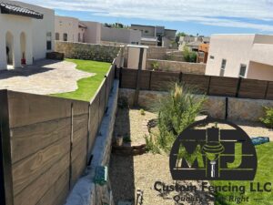 A long view of a custom wood fence on a stone retaining wall with desert landscaping by MJ Custom Fencing in Las Cruces, NM.