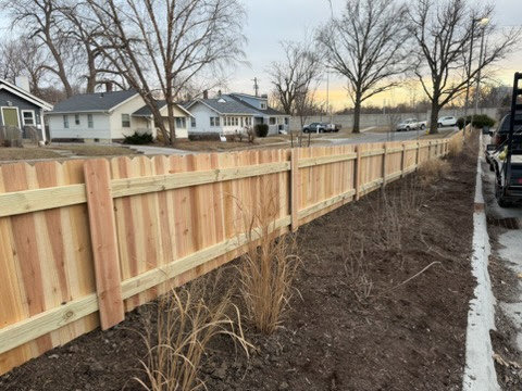 A long wooden picket fence installed along a street, a completed project by Top Rail Fence Des Moines in West Des Moines, IA.