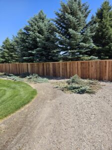 A long, sturdy wood privacy fence bordering a well-maintained yard and trees, expertly installed by Regan Fencing & Services in Nampa, ID.
