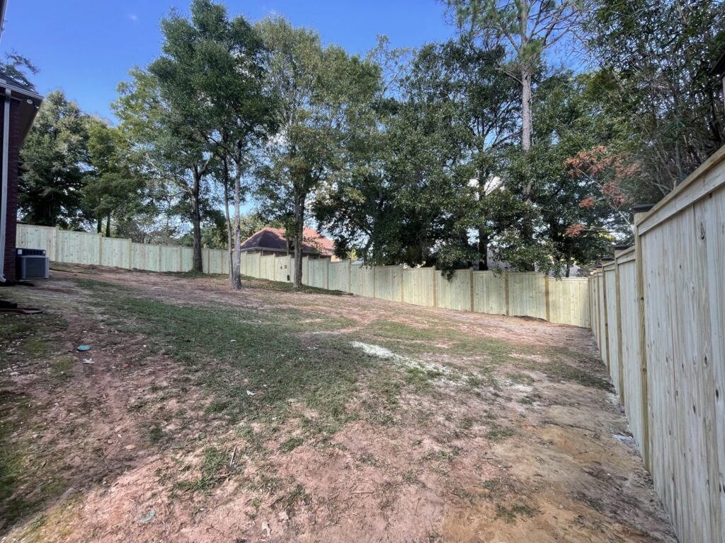 A long wooden privacy fence installed in a sloped residential backyard by Jaguar Fence LLC in Mobile, AL.