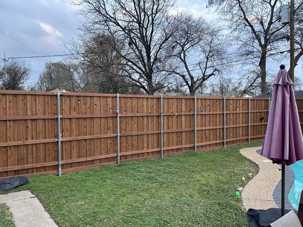 A long wooden privacy fence with sturdy metal posts, installed alongside a backyard pool by Reliable Texas Fencing in Fort Worth, TX.