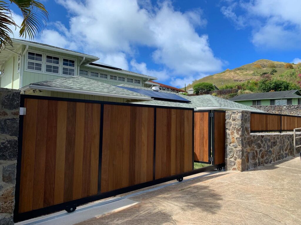 A long wooden slat fence with stone pillars and a matching sliding gate installed by A&D Services in Kapolei, HI.