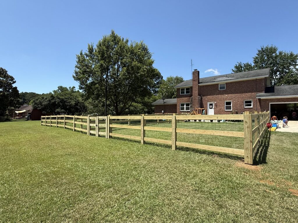 A long wood split-rail fence with wire mesh enclosing a large yard by Fence & Custom Gatework LLC in Columbia, SC