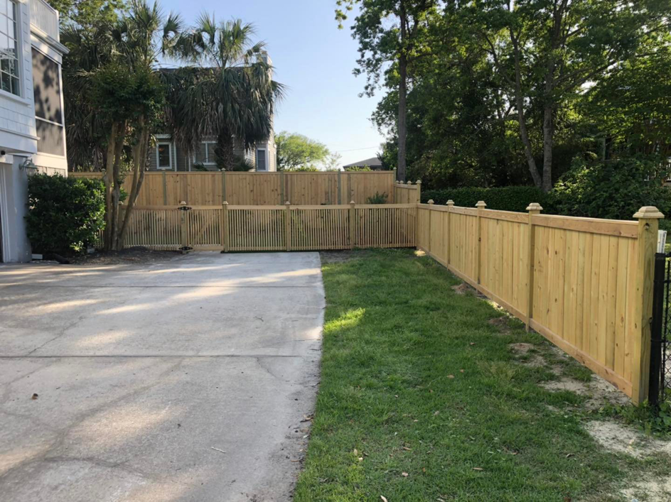 A long wooden fence line with a matching gate bordering a driveway, installed by Lowcountry Home Works843 LLC in Summerville, SC.