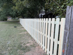 A long section of a newly installed wooden picket fence by Master Fence Builders in Fort Smith, AR, bordering a yard.