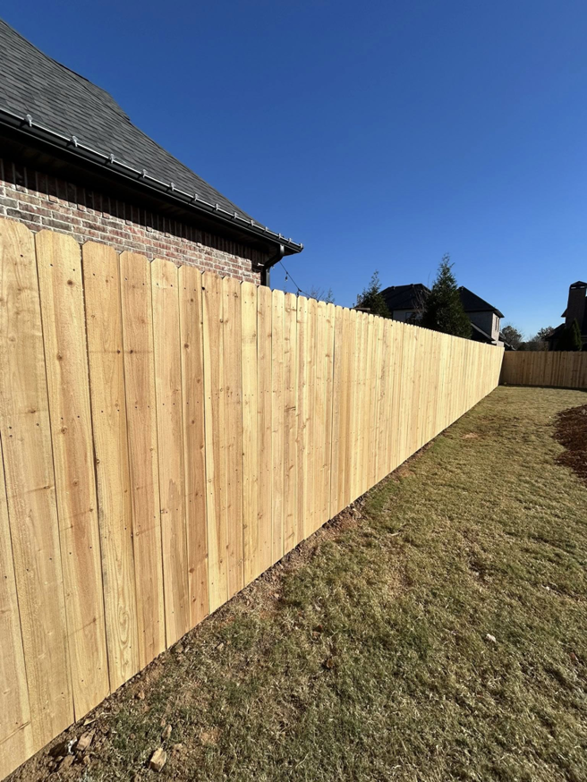 A long, newly installed wooden privacy fence enclosing a backyard by Timber Wolf Fence Co. in Rogers, AR.
