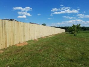 A long wooden privacy fence installed in a grassy field under a blue sky by DZS Fencing, LLC in Red Lion, PA.
