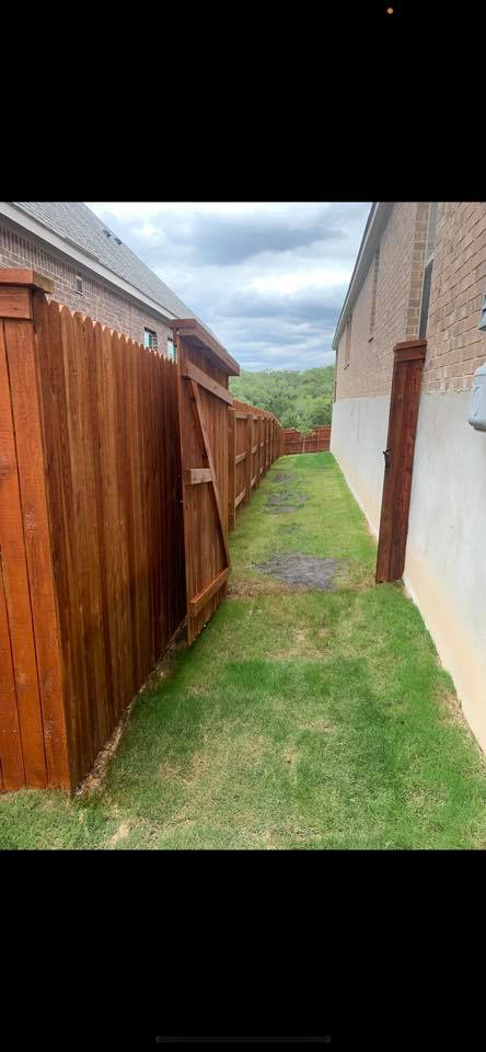 A long wooden privacy fence with a gate installed between two residential properties by G Squared Fencing & Services LLC in New Braunfels, TX.