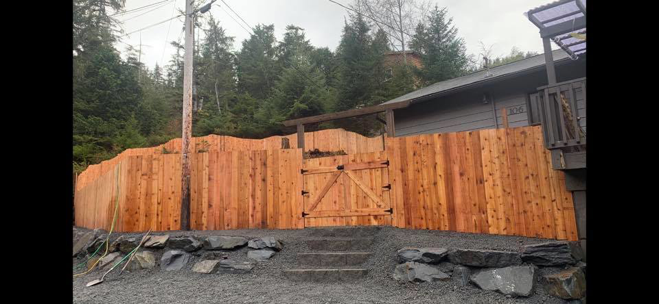 A long, newly installed wooden privacy fence with a gate, showcasing the work of Baranof Landscaping in Sitka, AK.