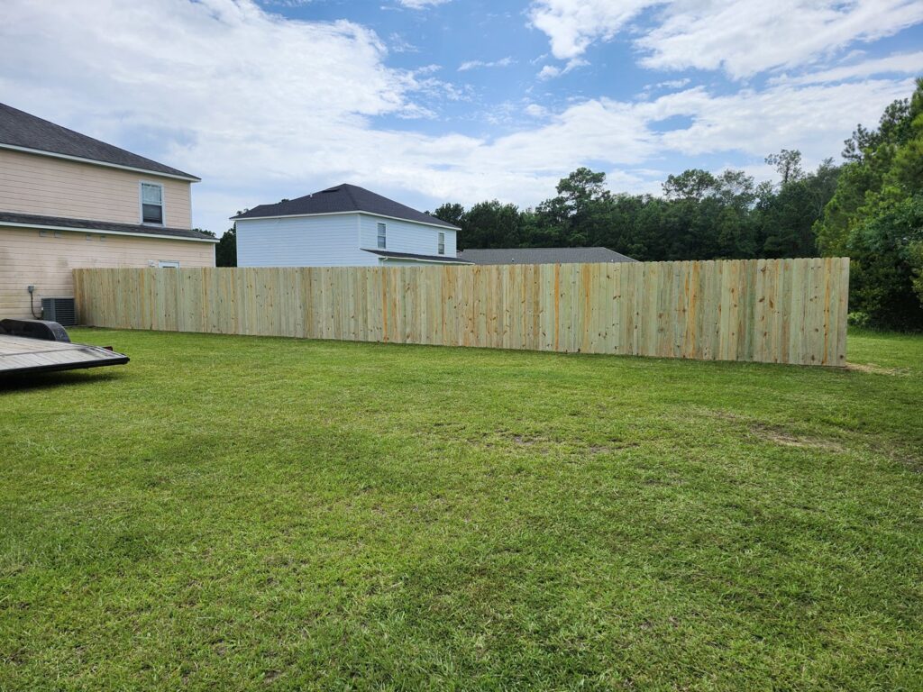 A long, newly installed wooden privacy fence in a residential backyard, ready for use, by Riggins Renovations LLC in Biloxi, MS.