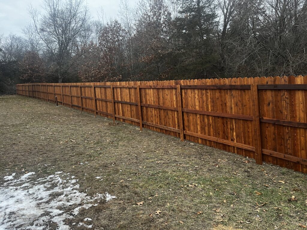 A long, stained wooden privacy fence installed in a semi-rural setting by Brothers Fence Co. in Madison, WI.