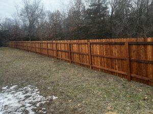 A long, stained wooden privacy fence installed in a semi-rural setting by Brothers Fence Co. in Madison, WI.