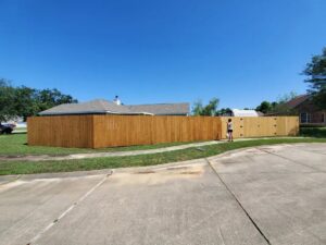 A long, newly installed wooden privacy fence with a gate, viewed from the street, by Riggins Renovations LLC in Biloxi, MS.