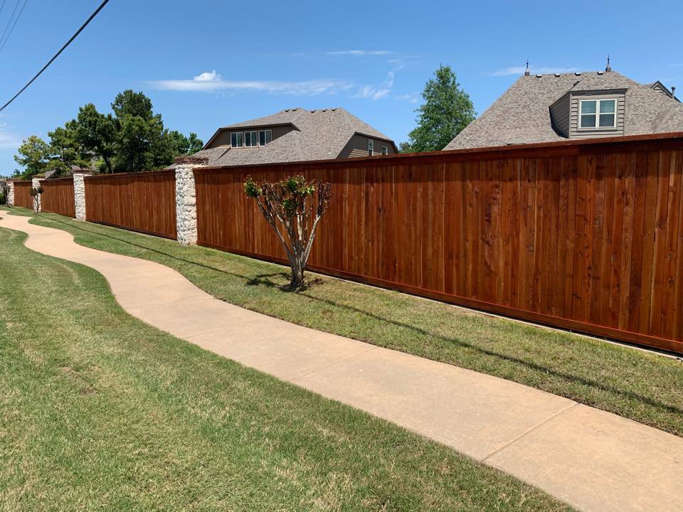 A long wooden privacy fence with decorative stone pillars installed by Ninety-One Services in Tulsa, OK
