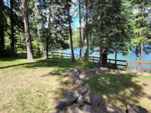 A long stretch of wooden fence with wire mesh installed along a scenic lakeside property by EcoGreen Fencing in Coeur d'Alene, ID.