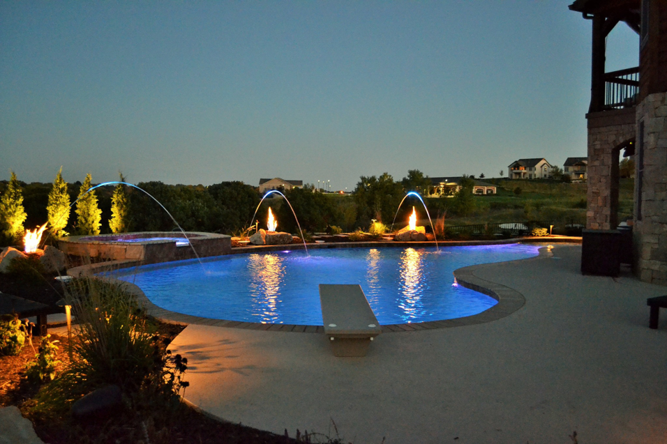A luxurious custom pool with fire and water features at night by Midwest Custom Pools, LLC in Lawrence, KS.