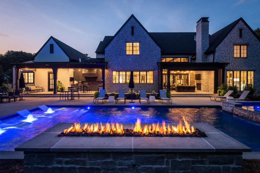 A luxury backyard pool with a glowing fire pit and blue lighting at dusk by Top Tier Pools in Franklin, TN.