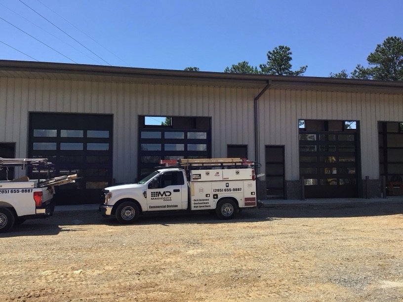 Magic City Door service trucks parked outside a commercial building with new glass garage doors in Birmingham, AL.