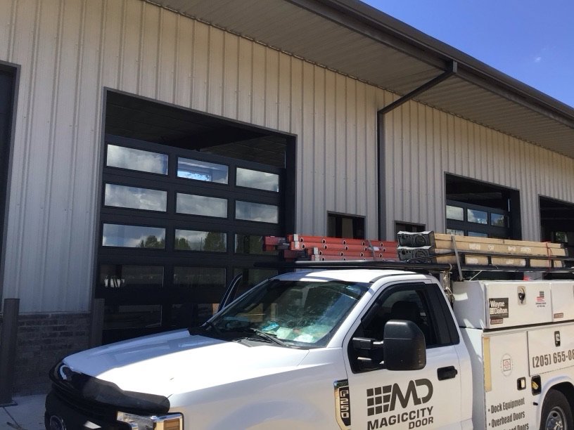 A Magic City Door service truck with ladders on site for a commercial glass garage door installation in Birmingham, AL.