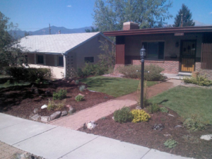 A well-maintained residential landscaping with mulch beds, various plants, and a green lawn by RMMLS in Colorado Springs, CO.