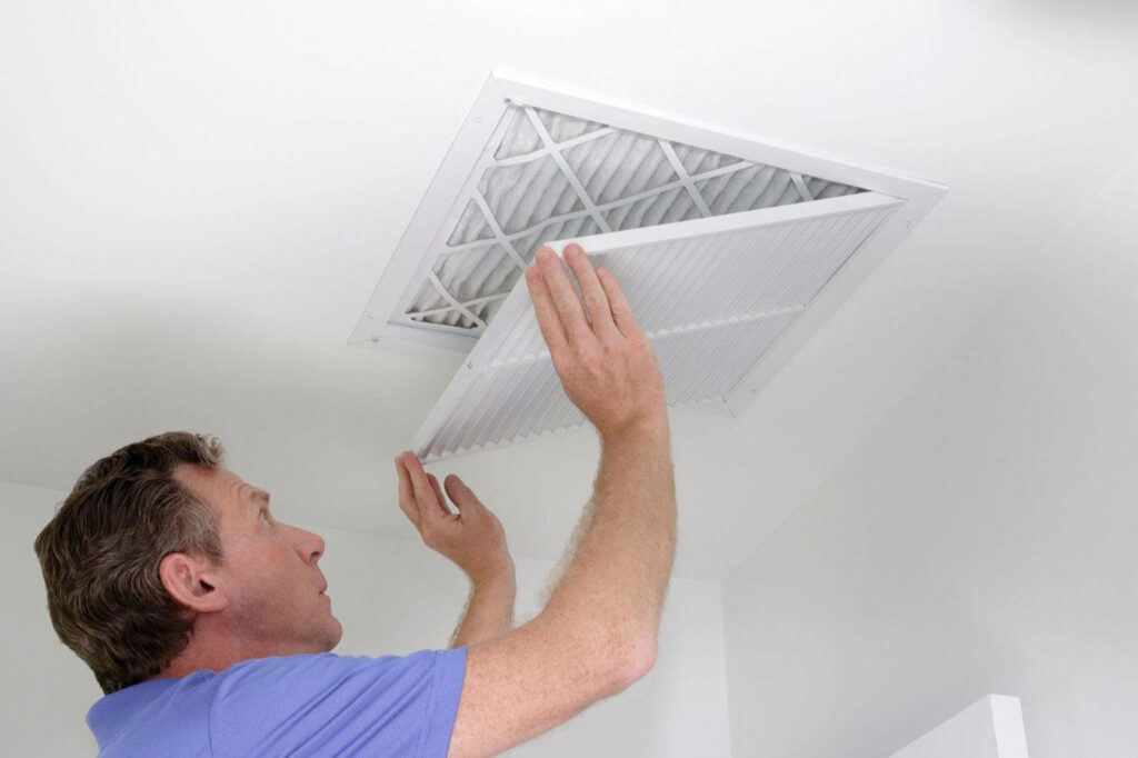 A man changing an air filter in a ceiling vent, a common HVAC maintenance task by Larry's Heating and Cooling, Inc. in Yankton, SD.