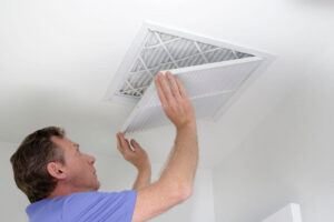 A man changing an air filter in a ceiling vent, a common HVAC maintenance task by Larry's Heating and Cooling, Inc. in Yankton, SD.