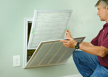 A man changing a dirty air filter in a wall return vent, performing HVAC maintenance for Alien Air Conditioning and Heating in Phoenix, AZ.