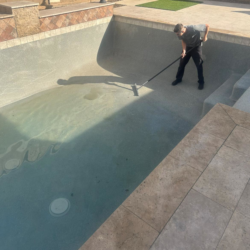 A man cleaning the bottom of an empty swimming pool for Porter Pool Service in Mesa, AZ