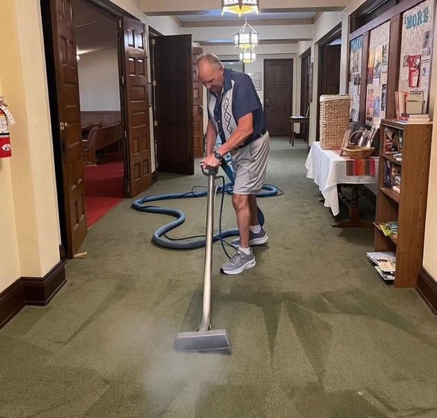 A man using a professional carpet cleaning machine to clean a green carpet in a hallway for Pichey's Clean Rite in Flint, MI.