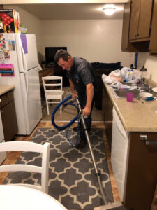 A man using a professional carpet cleaning wand to clean a rug in a kitchen, performed by Utah Carpet Systems in Orem, UT.