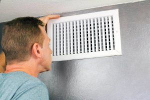 A technician from All Comfort Air Heating and Air Conditioning inspecting an air vent in Raleigh, NC.