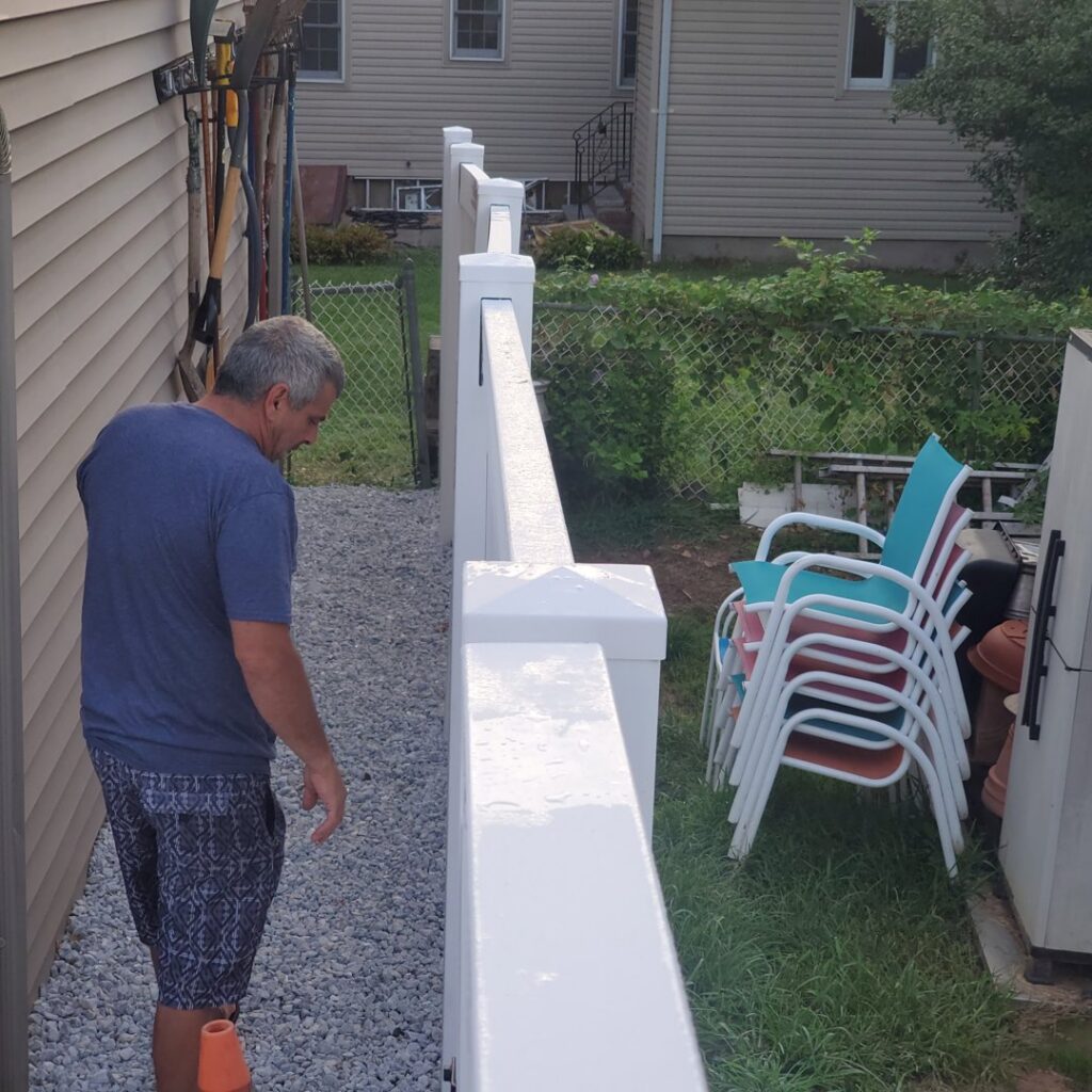 A man inspecting a newly installed white vinyl fence, demonstrating attention to detail by Fox Fence Enterprises Inc in Clifton, NJ.