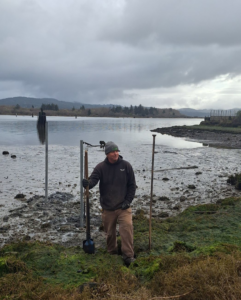 A man installing fence posts in a muddy area near water, a Fencing Contractor job by West Coast Fencing in Coos Bay, OR.