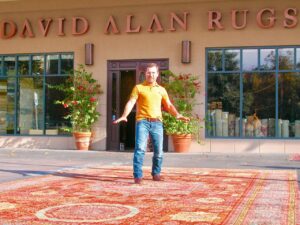 A man standing on a large red area rug displayed outside the David Alan Rugs storefront in Austin, TX.