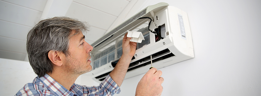 A technician repairing an indoor air conditioning unit for Woodcock & Armani Mechanical Contractors in East Syracuse, NY.