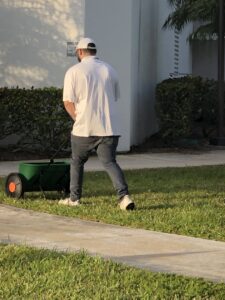 A man spreading lawn treatment with a spreader, a service offered by Globe Pest Inc in Miami, FL.