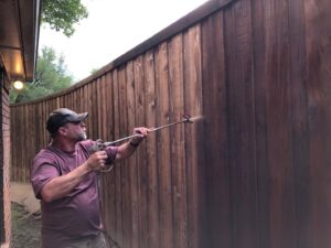 A professional staining a wood fence with a sprayer for Texas Tuff Stain and Seal in Fort Worth, TX.
