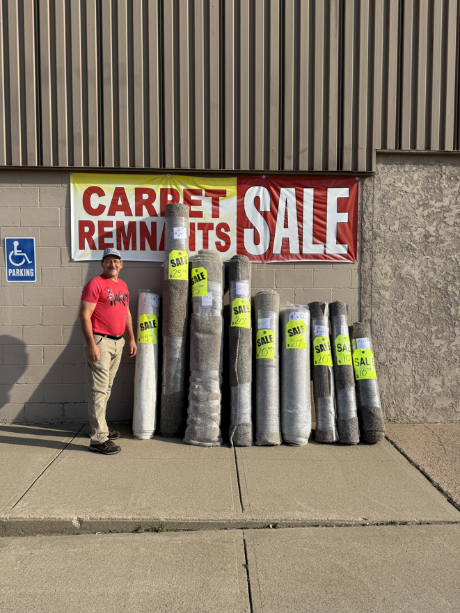 A man standing proudly next to rolls of carpet remnants for sale at Mozak's Floors & More in Yankton, SD