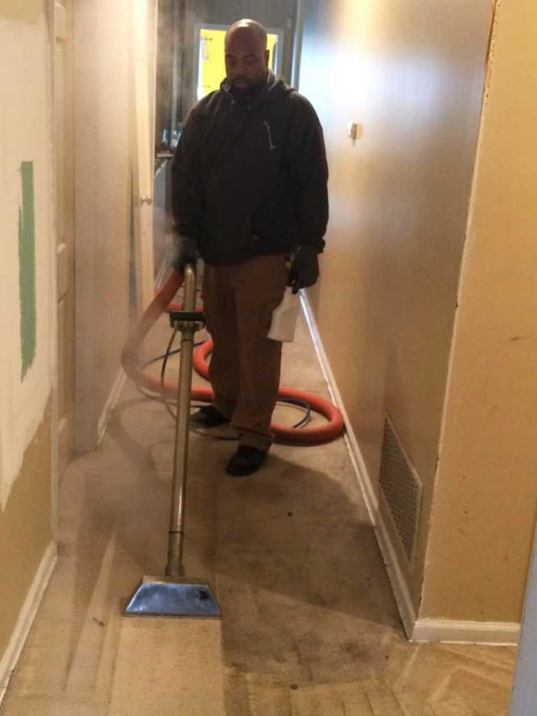A man steam cleaning a carpet in a narrow hallway, a service from Harper's Carpet & Upholstery Cleaning in San Antonio, FL.