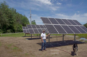 A man standing next to newly installed ground-mounted solar panels by Metruk's Electrical Contracting, Inc. in Underhill, VT.