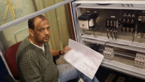 A man reviewing a wiring diagram while working on an electrical control panel for D-America Electrical Contractor LLC in Passaic, NJ.