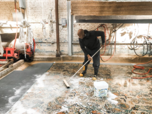 A worker manually scrubbing a large rug with soap and water at George Bell Rug Cleaning & Restoration in Jackson, MS.