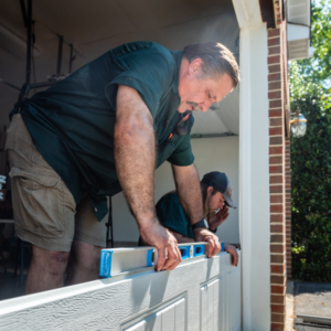 Two contractors installing a new garage door panel with a level at Annapolis Garage Doors Inc. in Annapolis, MD.