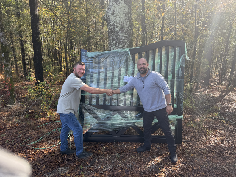 Two men shaking hands in front of a newly delivered black metal gate by All With Us LLC in Green Cove Springs, FL.