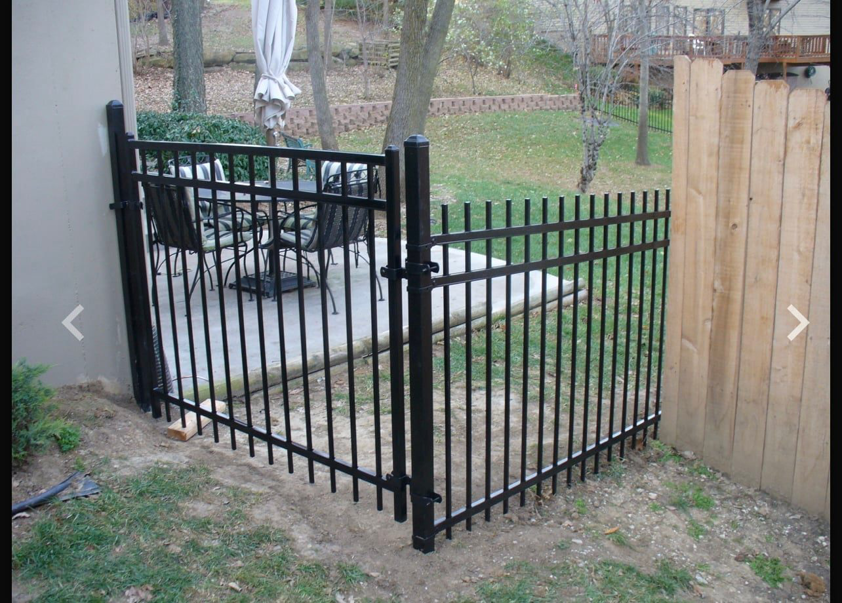 A durable black metal fence gate and adjacent wooden fence section installed by Pokey Fencing & Masonry in Stillwater, OK.