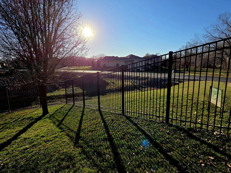 A black metal fence installed on a sunny day, featuring a Green Acres Fence Co sign in Salina, KS.